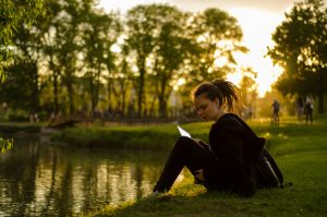 Studentica čita knjigu sjedeći uz rijeku u parku